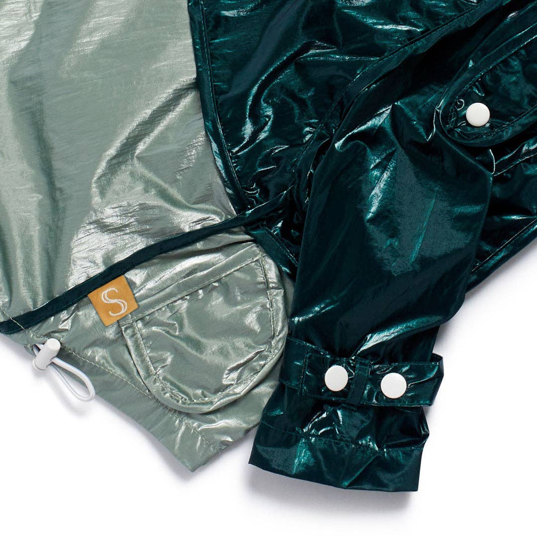 Close-up of a shiny green raincoat with a pocket and white buttons on a white background.
