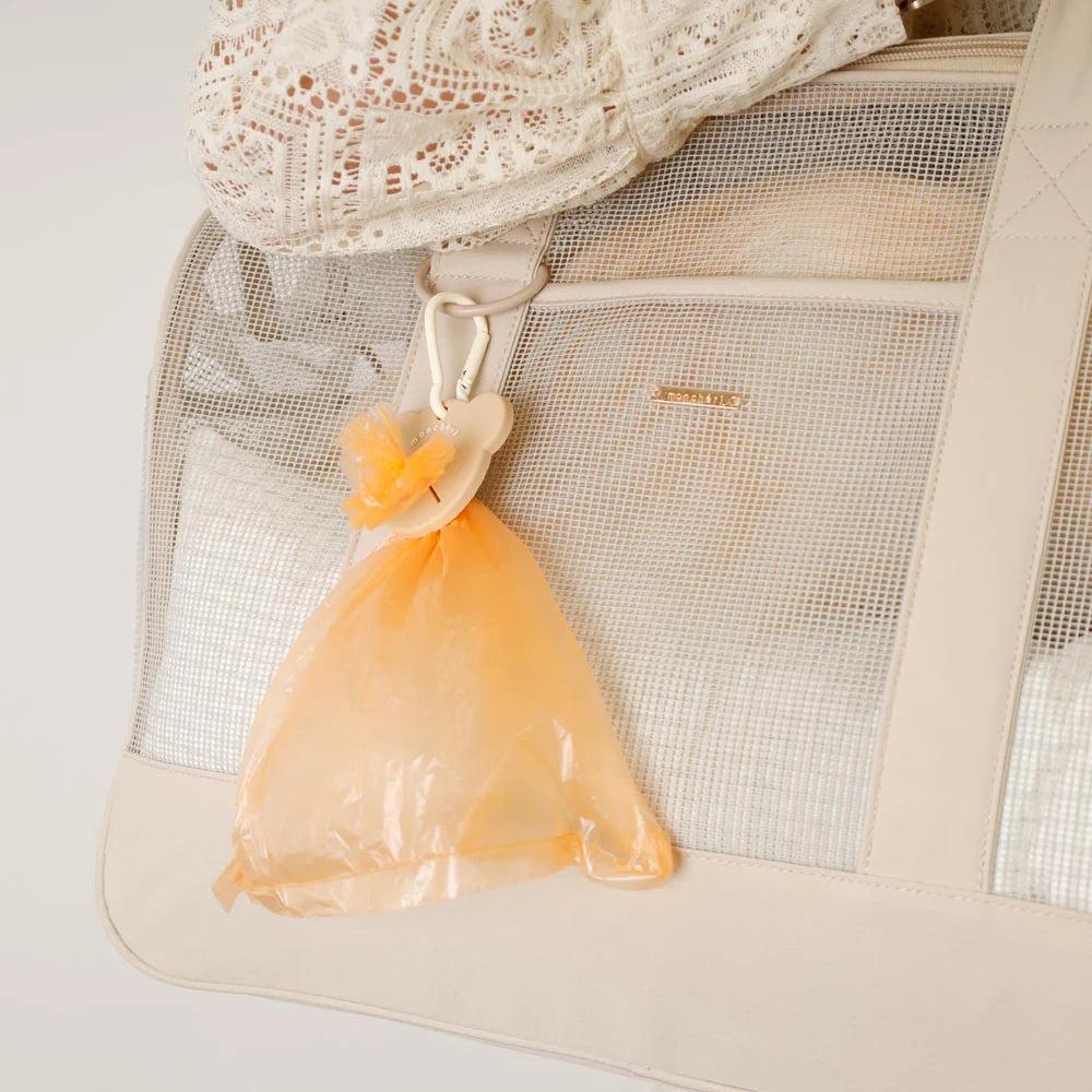 Beige dog poop bag holder with an orange poop bag secured onto a beige mesh dog carrier