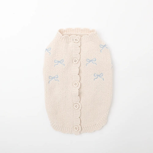 Beige knitted dog sweater with button details and small blue bow patterns on a white background