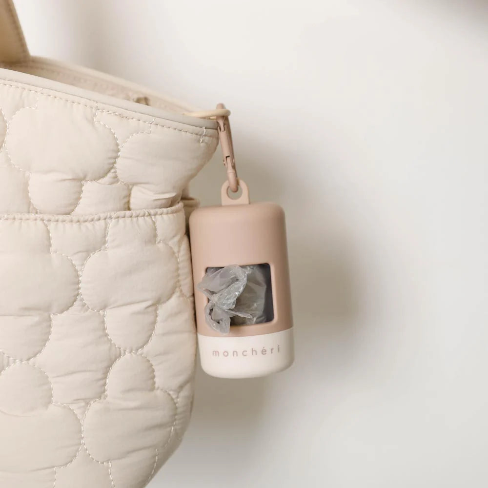 Beige plastic dog poop bag holder attached to a beige quilted bag on a white background