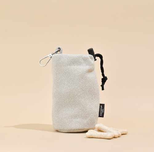 Light beige tweed drawstring dog treat pouch with a carabiner on a beige background